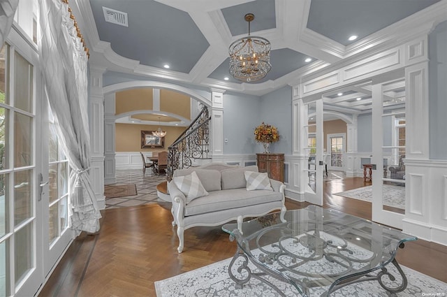 living room featuring coffered ceiling, dark parquet floors, a notable chandelier, decorative columns, and crown molding