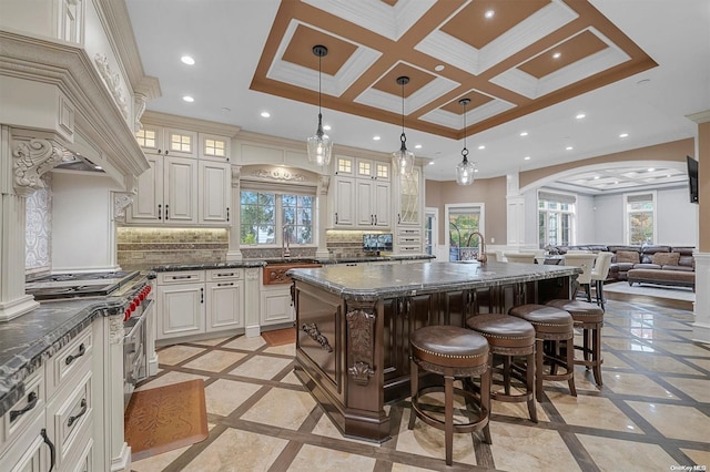 kitchen with tasteful backsplash, high end stainless steel range oven, decorative light fixtures, dark stone countertops, and an island with sink