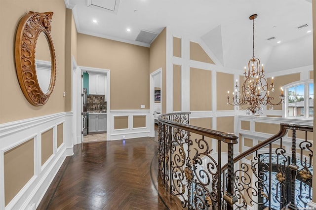 hall featuring dark parquet flooring, an inviting chandelier, high vaulted ceiling, and ornamental molding