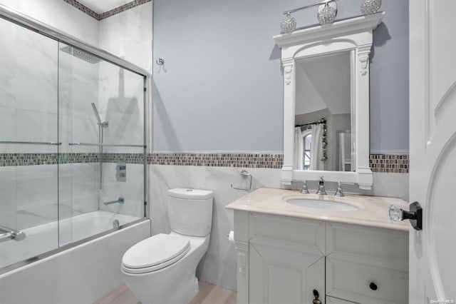 full bathroom with combined bath / shower with glass door, vanity, toilet, and tile walls