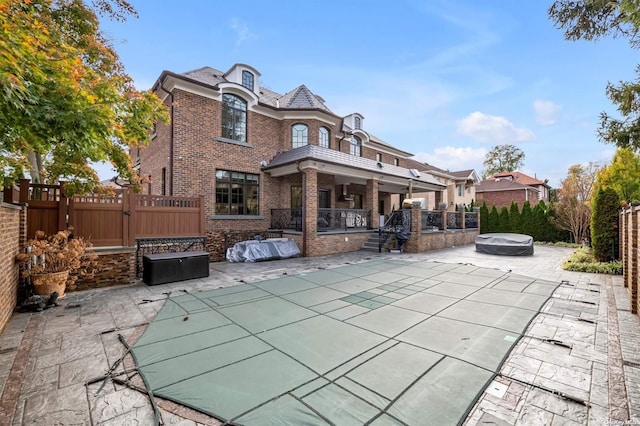 rear view of property with a pool with hot tub and a patio area