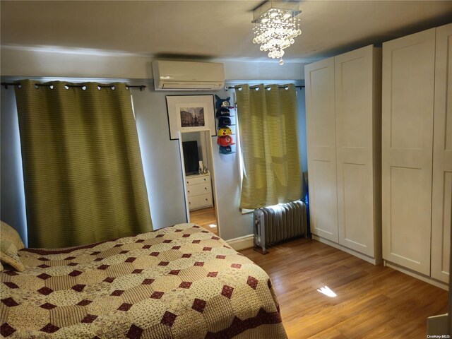 unfurnished bedroom featuring a notable chandelier, light wood-type flooring, an AC wall unit, and radiator