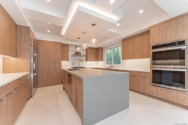 kitchen with a kitchen island with sink, appliances with stainless steel finishes, decorative backsplash, a tray ceiling, and sink