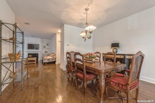 dining space featuring built in features, an inviting chandelier, and dark wood-type flooring