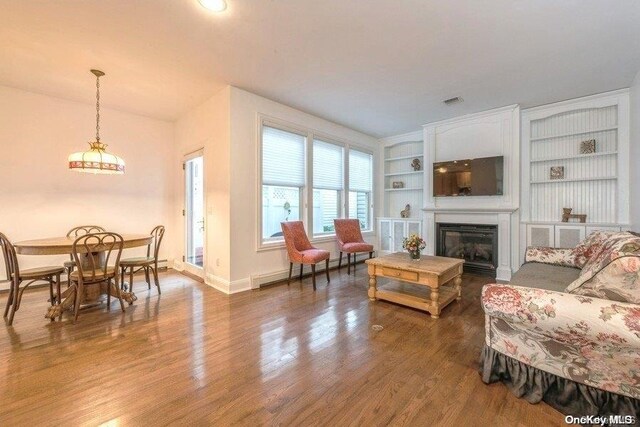 living room with dark wood-type flooring, built in features, and a baseboard heating unit