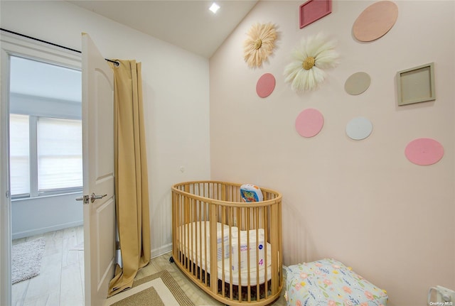 bedroom with light hardwood / wood-style flooring, a nursery area, and lofted ceiling