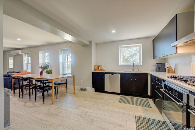 kitchen featuring appliances with stainless steel finishes, light wood-type flooring, wall chimney exhaust hood, sink, and an AC wall unit