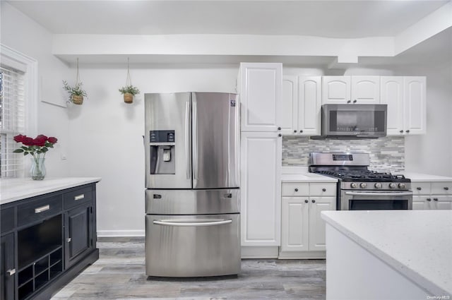 kitchen with stainless steel appliances, white cabinetry, backsplash, and light wood-type flooring