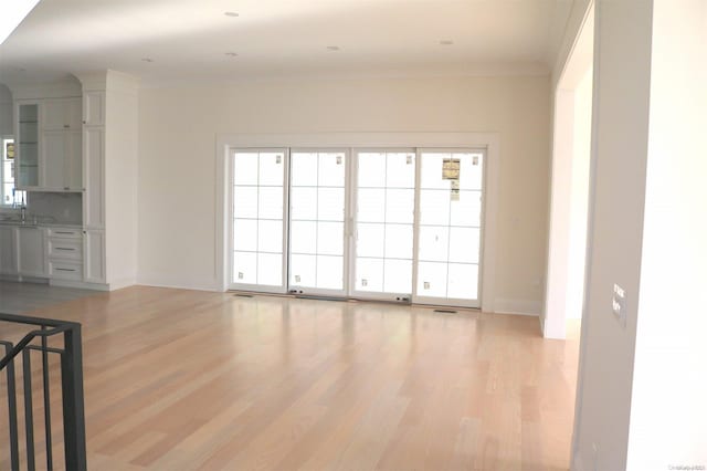 unfurnished living room featuring light hardwood / wood-style floors, crown molding, and sink