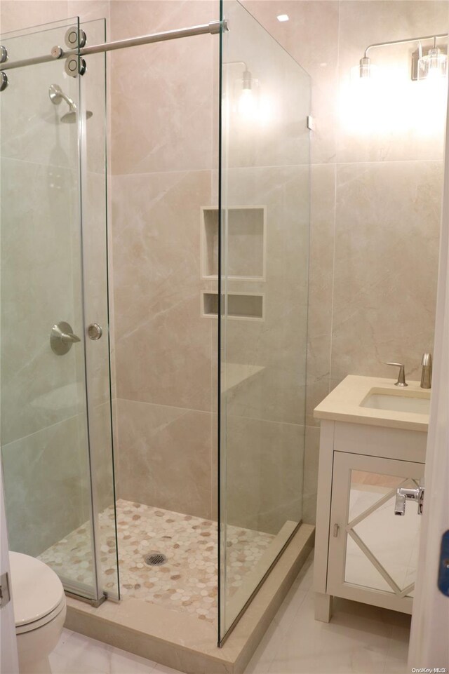 bathroom with toilet, vanity, tile walls, and walk in shower