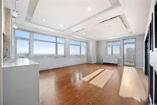 unfurnished living room with light hardwood / wood-style floors, sink, a wealth of natural light, and a tray ceiling