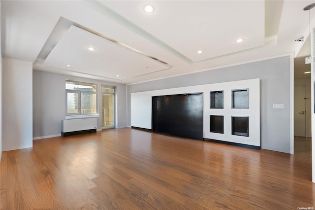 unfurnished living room featuring hardwood / wood-style floors, radiator heating unit, and a raised ceiling