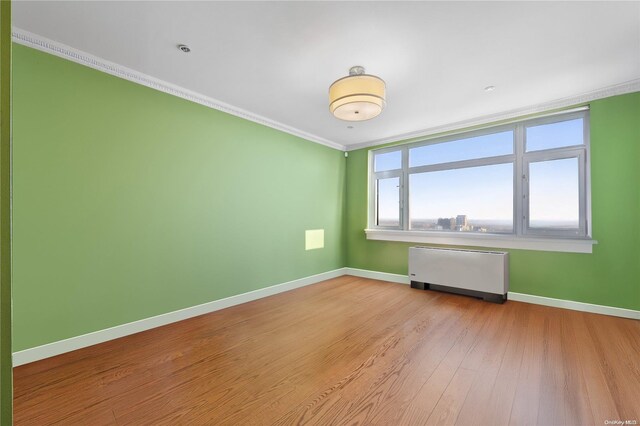 unfurnished room with radiator heating unit, ornamental molding, and light hardwood / wood-style flooring