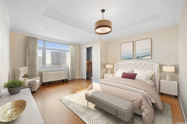 bedroom featuring radiator heating unit, light wood-type flooring, a raised ceiling, and crown molding