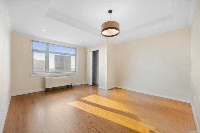 spare room with hardwood / wood-style flooring, radiator, crown molding, and a tray ceiling