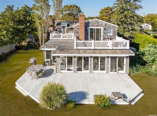 rear view of house featuring a lawn, a wooden deck, a balcony, and a playground