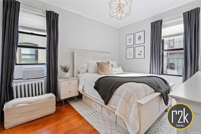 bedroom with wood-type flooring, radiator heating unit, ornamental molding, and an inviting chandelier