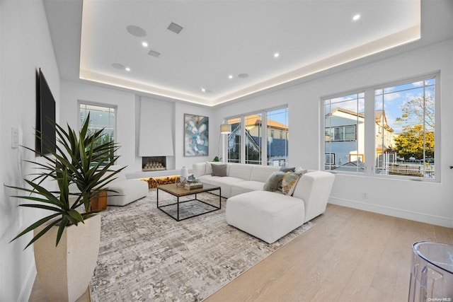 living room with a raised ceiling, a large fireplace, and light hardwood / wood-style flooring