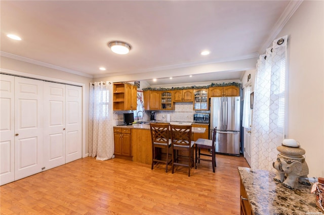 kitchen with stainless steel refrigerator, tasteful backsplash, light hardwood / wood-style flooring, a kitchen bar, and ornamental molding