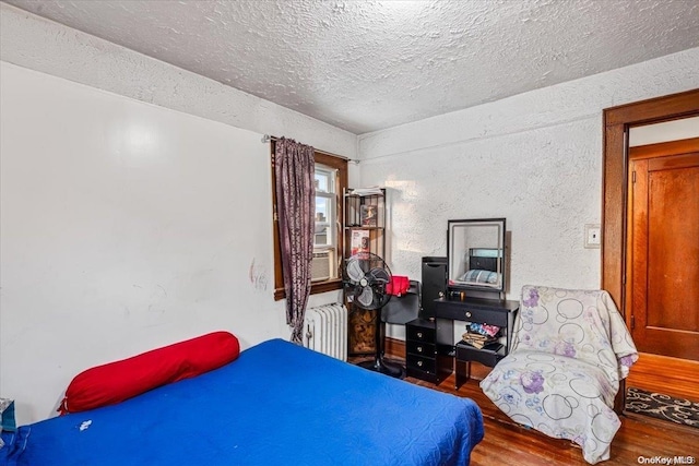 bedroom featuring radiator heating unit, a textured ceiling, hardwood / wood-style flooring, and cooling unit