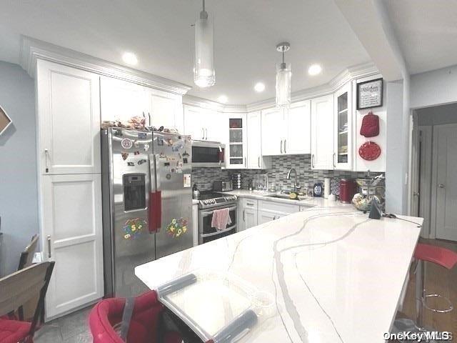 kitchen with a breakfast bar, white cabinets, sink, hanging light fixtures, and appliances with stainless steel finishes