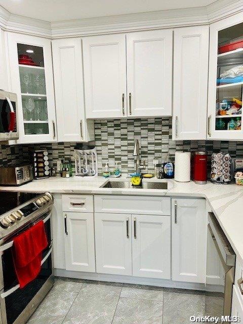 kitchen featuring decorative backsplash, appliances with stainless steel finishes, sink, light tile patterned floors, and white cabinets