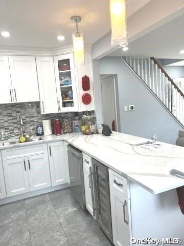 kitchen featuring backsplash, white cabinets, sink, stainless steel dishwasher, and decorative light fixtures