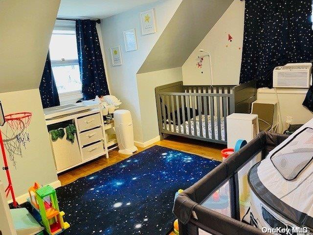 bedroom with a crib, hardwood / wood-style floors, and cooling unit