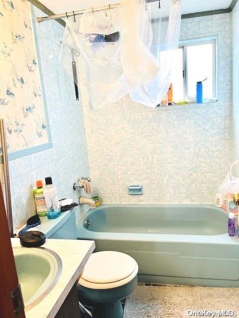 full bathroom with vanity, toilet, tiled shower / bath, and tile walls