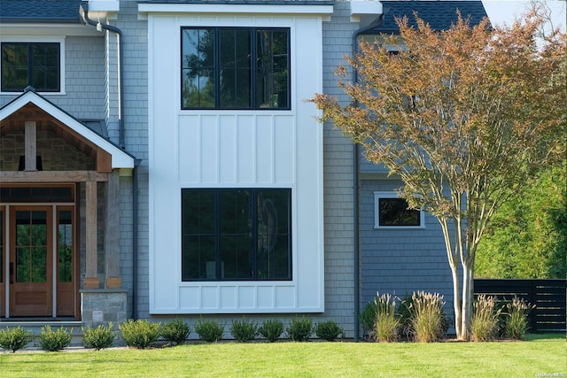 view of side of property with board and batten siding, a shingled roof, and a yard