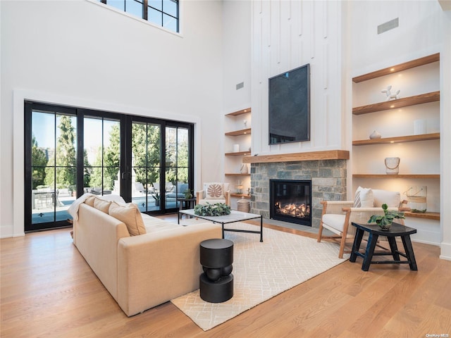 living room with a stone fireplace, a healthy amount of sunlight, visible vents, and wood finished floors