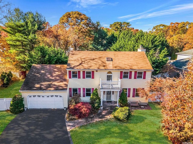 colonial inspired home featuring a front lawn, aphalt driveway, an attached garage, a balcony, and a chimney
