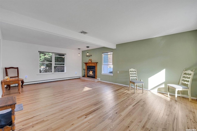 unfurnished living room featuring baseboard heating, beamed ceiling, a healthy amount of sunlight, and light hardwood / wood-style floors