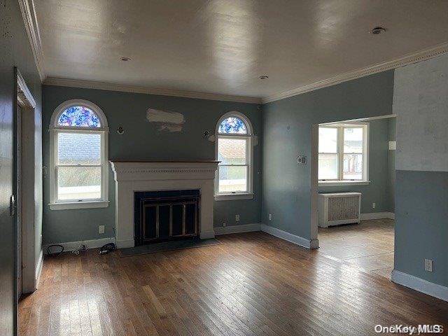 unfurnished living room with hardwood / wood-style flooring, radiator heating unit, and crown molding