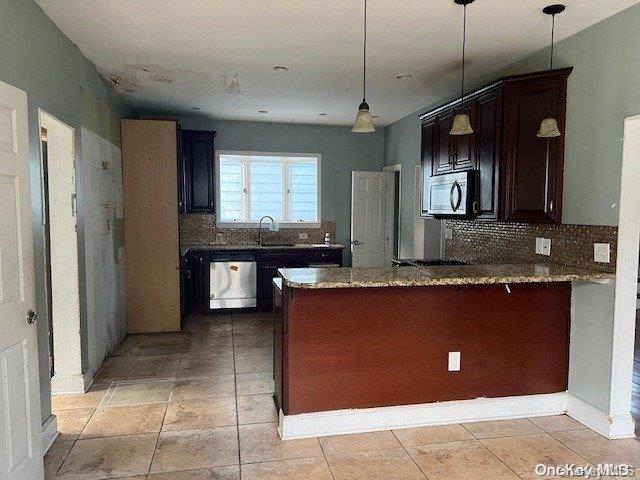 kitchen with kitchen peninsula, light stone counters, dark brown cabinetry, dishwasher, and hanging light fixtures