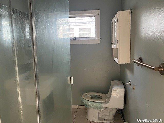 bathroom with tile patterned flooring, an enclosed shower, and toilet