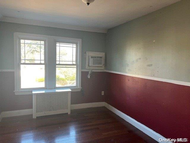 spare room featuring radiator, dark hardwood / wood-style flooring, a wall mounted air conditioner, and ornamental molding