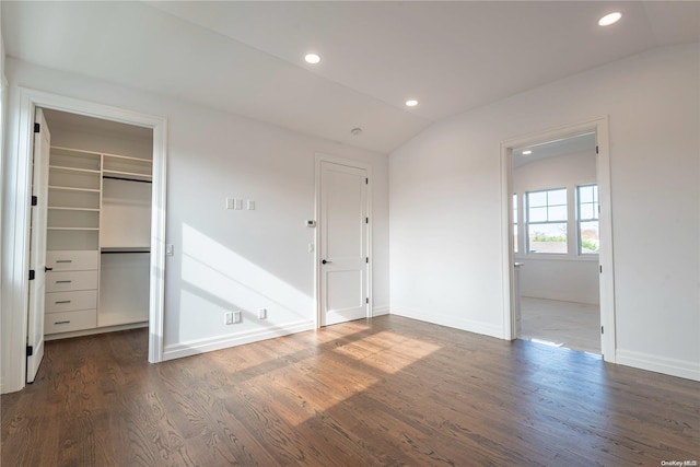 unfurnished bedroom with a walk in closet, a closet, dark hardwood / wood-style flooring, and lofted ceiling