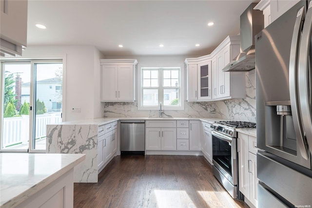 kitchen featuring white cabinets, appliances with stainless steel finishes, light stone countertops, and wall chimney range hood