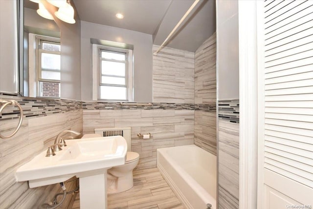 bathroom with a washtub, toilet, and tile walls