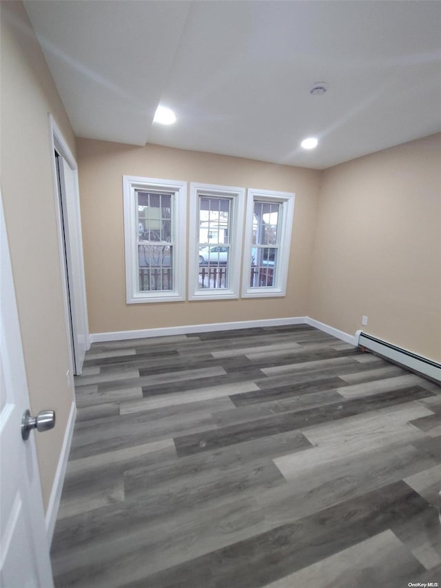 empty room featuring dark wood-type flooring and a baseboard heating unit