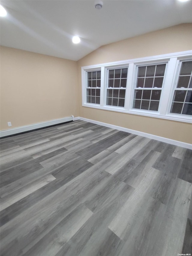 empty room featuring hardwood / wood-style flooring, a baseboard radiator, and vaulted ceiling