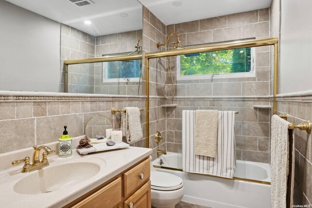 full bathroom featuring backsplash, toilet, shower / bath combination with glass door, vanity, and tile walls