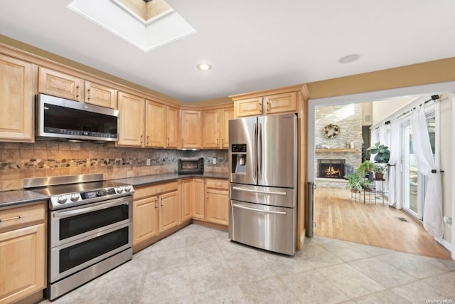 kitchen with light brown cabinets, light hardwood / wood-style flooring, decorative backsplash, a fireplace, and appliances with stainless steel finishes