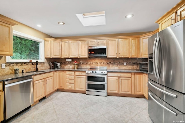 kitchen featuring appliances with stainless steel finishes, light brown cabinetry, a skylight, tasteful backsplash, and sink