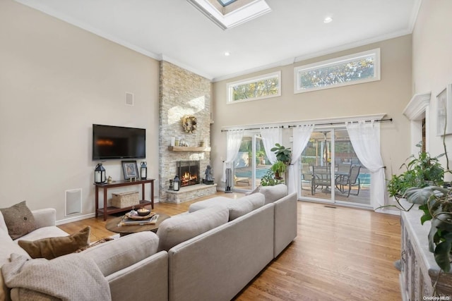 living room featuring a skylight, ornamental molding, light hardwood / wood-style flooring, a fireplace, and a high ceiling