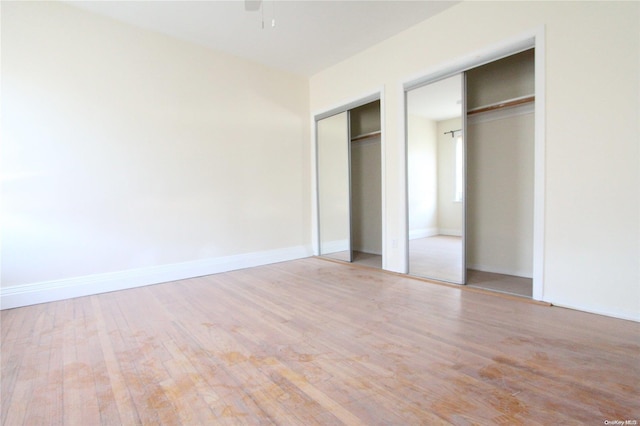 unfurnished bedroom featuring light wood-type flooring and multiple closets