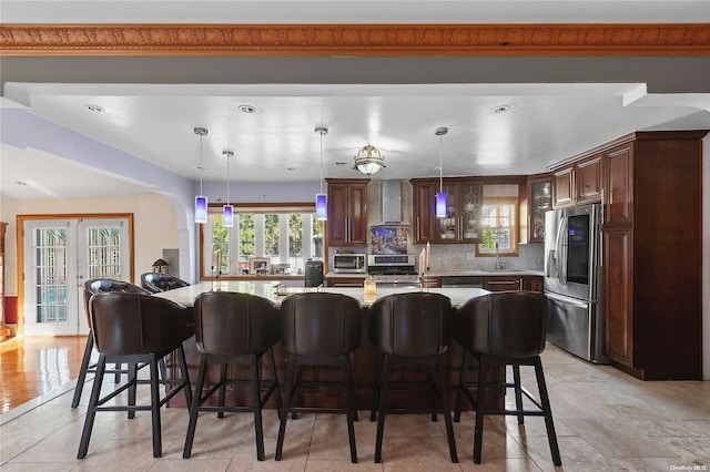 kitchen featuring a large island with sink, wall chimney exhaust hood, decorative backsplash, a kitchen bar, and stainless steel appliances