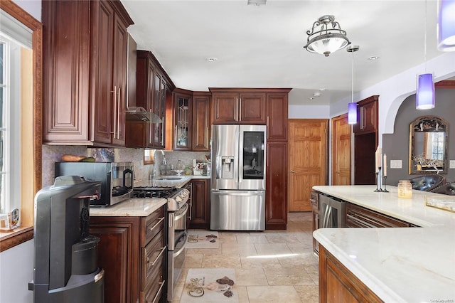 kitchen featuring sink, light stone countertops, appliances with stainless steel finishes, tasteful backsplash, and decorative light fixtures