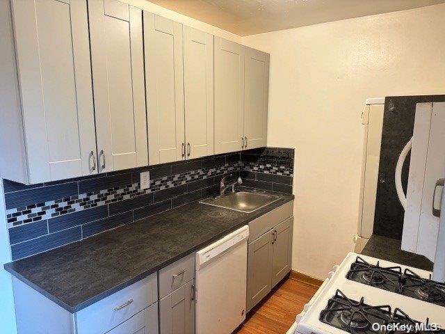 kitchen featuring light wood-type flooring, white appliances, backsplash, and sink